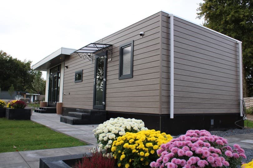 Moderne vakantiewoning met een stijlvolle gevel, omringd door bloeiende chrysanten en een betegeld pad.