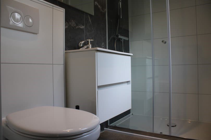 Moderne badkamer met een hangend toilet, wastafel met lade en inloopdouche met glazen wand
