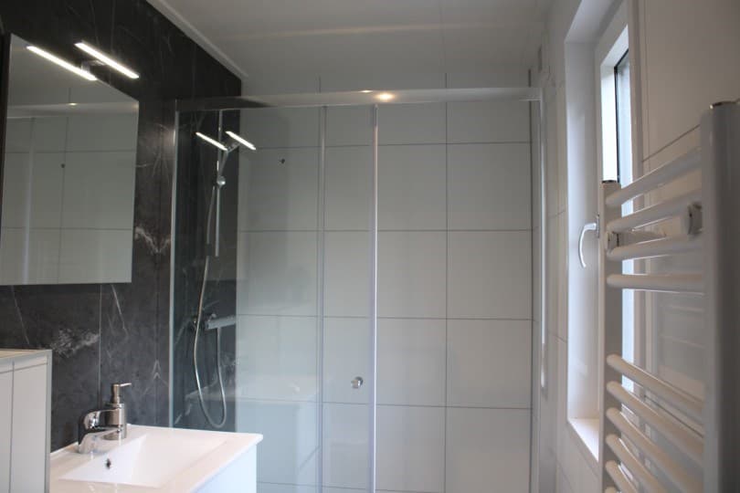 Moderne badkamer met inloopdouche, wastafel en verwarmingselement aan de wand.