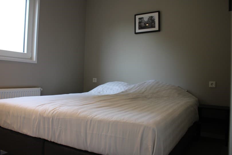 Slaapkamer met een groot bed, een radiator en een raam met zicht op buiten. Aan de wand hangt een foto.