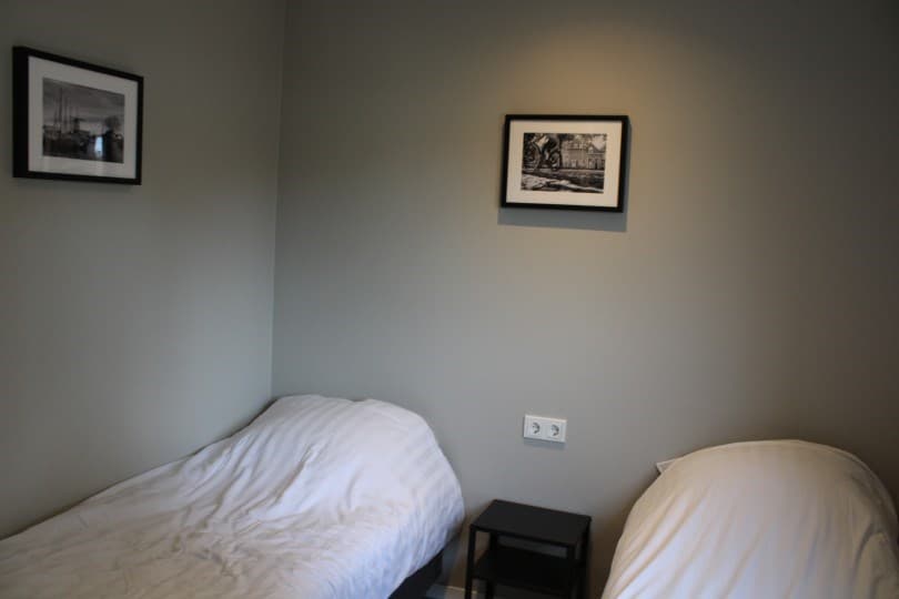 Slaapkamer met twee eenpersoonsbedden, nachtkastje en twee ingelijste zwart-wit foto’s aan de muur.