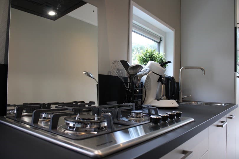Keuken met gasfornuis, een waterkoker en keukengerei op het aanrecht, lichtinval vanuit het raam