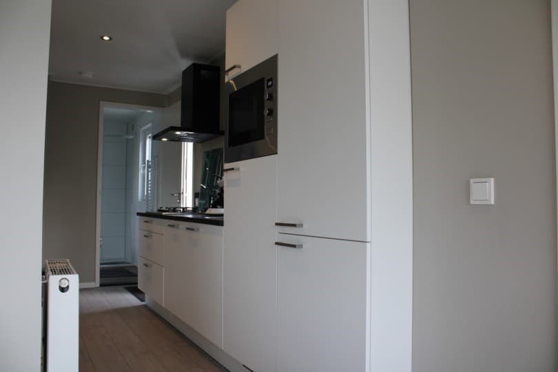 Moderne keuken met witte kasten, gasfornuis, oven en een radiator aan de muur in een lichte kamer.