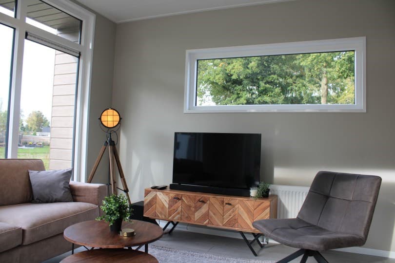 Moderne woonkamer met een tv-meubel, een bank, een fauteuil en een groot raam met uitzicht op groen.
