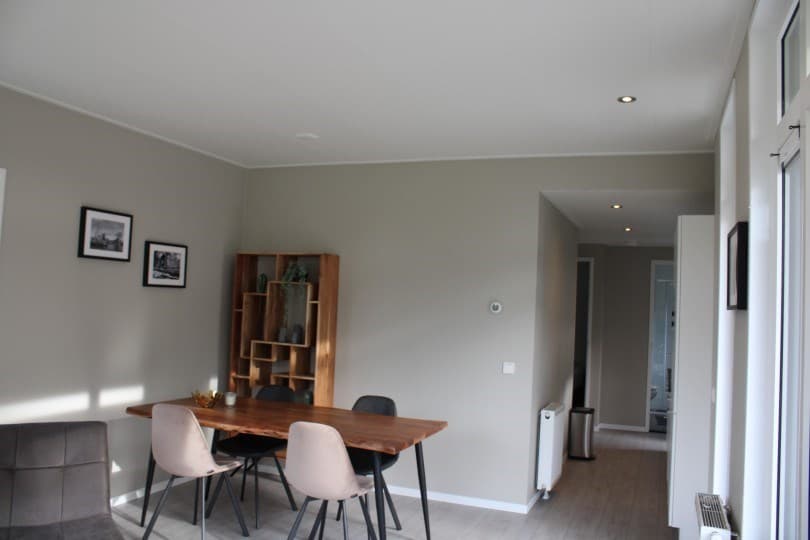 Eethoek met houten tafel en stoelen, grijze muren en moderne wanddecoratie in lichte, ruime kamer.