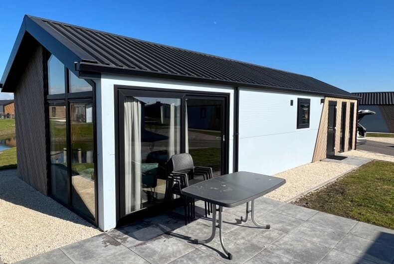 Moderne vakantiewoning met glasfacade, terras en tafel, gelegen in een groene omgeving met bestrating.