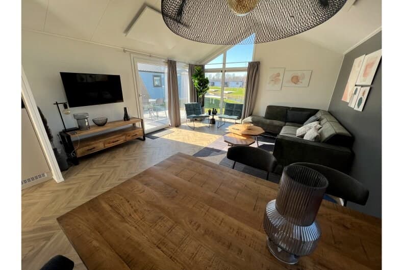 Moderne woonkamer met zithoek, eettafel en grote ramen met uitzicht op groen landschap en buitenmeubilair.