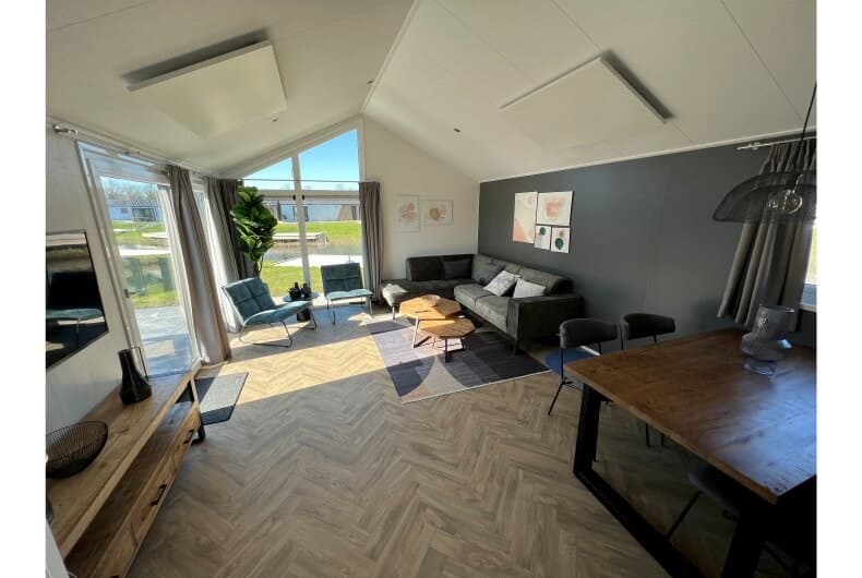 Lichte woonkamer met grote ramen, comfortabele zitplaatsen, een eettafel en moderne inrichting in een vakantiehuis.