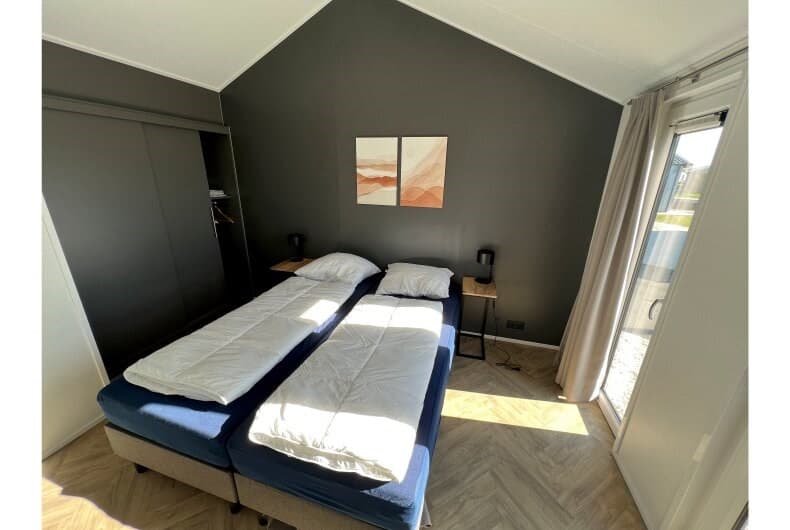 Slaapkamer met twee afzonderlijke bedden, nachtkastjes en een wandkast in een vakantiehuis.