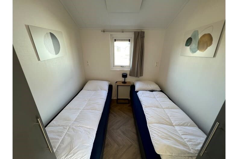 Slaapkamer met twee eenpersoonsbedden, nachtstaander en kunstwerken aan de muur, raam met gordijnen.