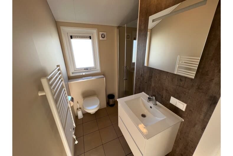 Moderne badkamer met douche, wastafel, spiegel en raam met uitzicht op de buitenruimte.
