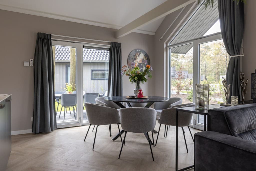 Gezellige eetruimte met ronde tafel, stoelen en grote ramen die uitkijken op de tuin van Vakantiepark Latour te Oirschot