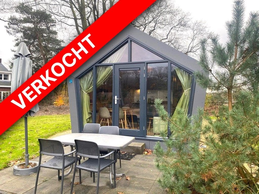 Moderne vakantiewoning met grote ramen, een terras en buitentafel, omgeven door bomen en groen.