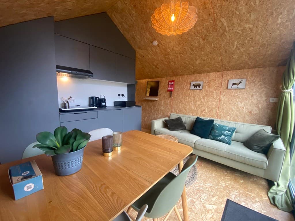 Moderne woonkamer met een open keuken, houten muren, een eettafel en een comfortabele bank met groene gordijnen.