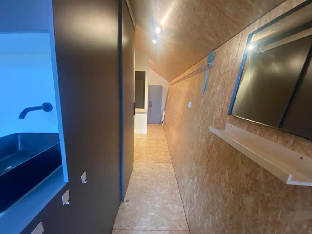 Langgerekte gang met houten wandpanelen, zwart aanrecht en een spiegel aan de muur, met toegang tot andere ruimtes.