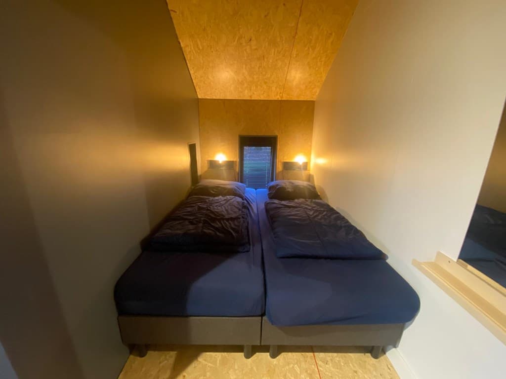 Slaapkamer met twee aparte bedden, lampen aan weerszijden en een raam met verduistering in een rustige omgeving