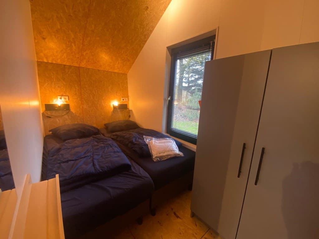 Sfeervolle slaapkamer met twee aparte bedden, nachtlampjes en een kast naast grote ramen met uitzicht op buiten.