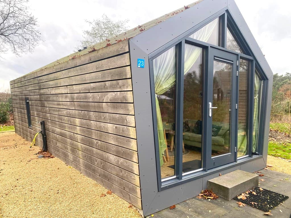 Moderne vakantiewoning met houten gevel en grote glazen pui, gelegen in een groene omgeving
