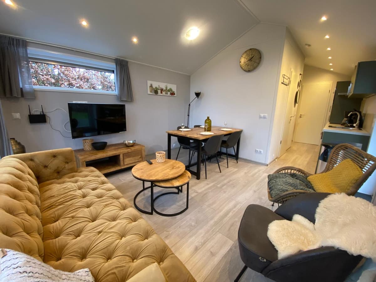 Woonkamer met een bank, eettafel, stoelen en televisie, lichte wanden en moderne inrichting