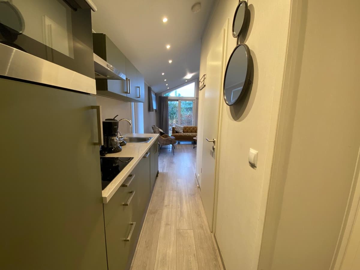 Ingang van een woning met een keuken aan de linkerzijde en een zitgedeelte met uitzicht op de tuin aan de rechterzijde.