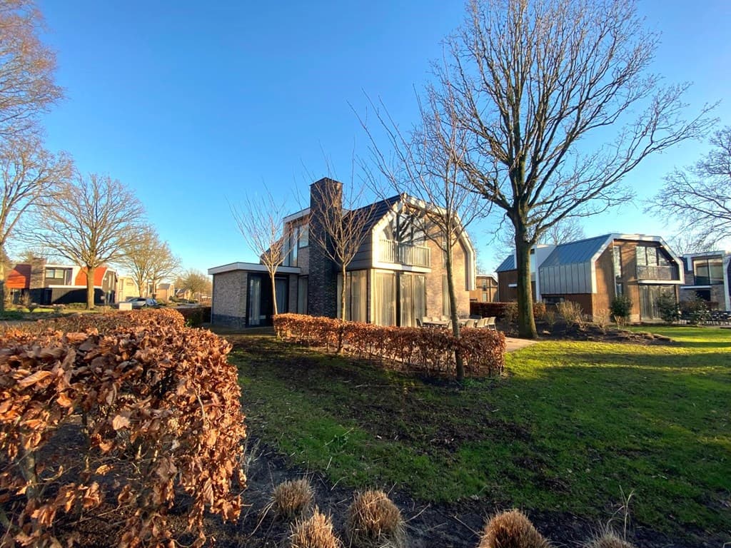 Moderne vakantiewoning met grote ramen, omringd door bomen en een grasveld, gelegen in EuroParcs Zuiderzee.