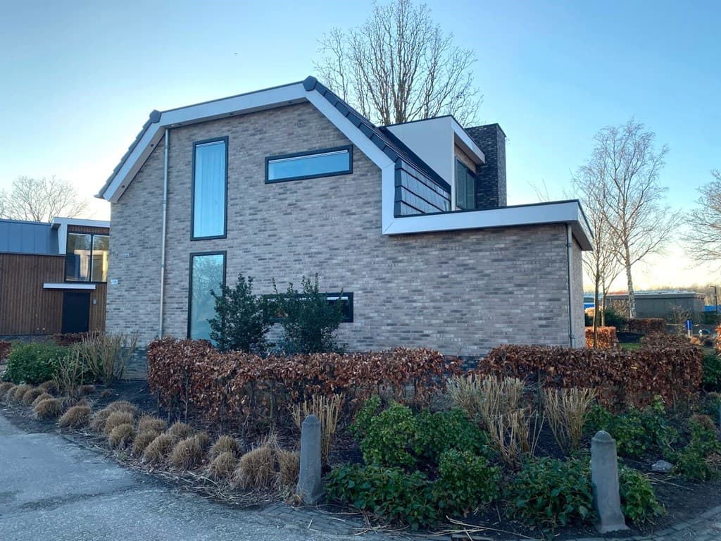 Moderne vakantiewoning met een bakstenen gevel, grote ramen en aangelegde tuin met groen en hagen