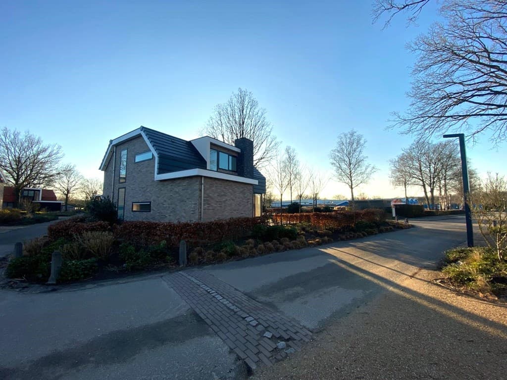 Moderne woning met een lichtgekleurde gevel, omringd door bomen en een half-verhard pad in EuroParcs Zuiderzee.