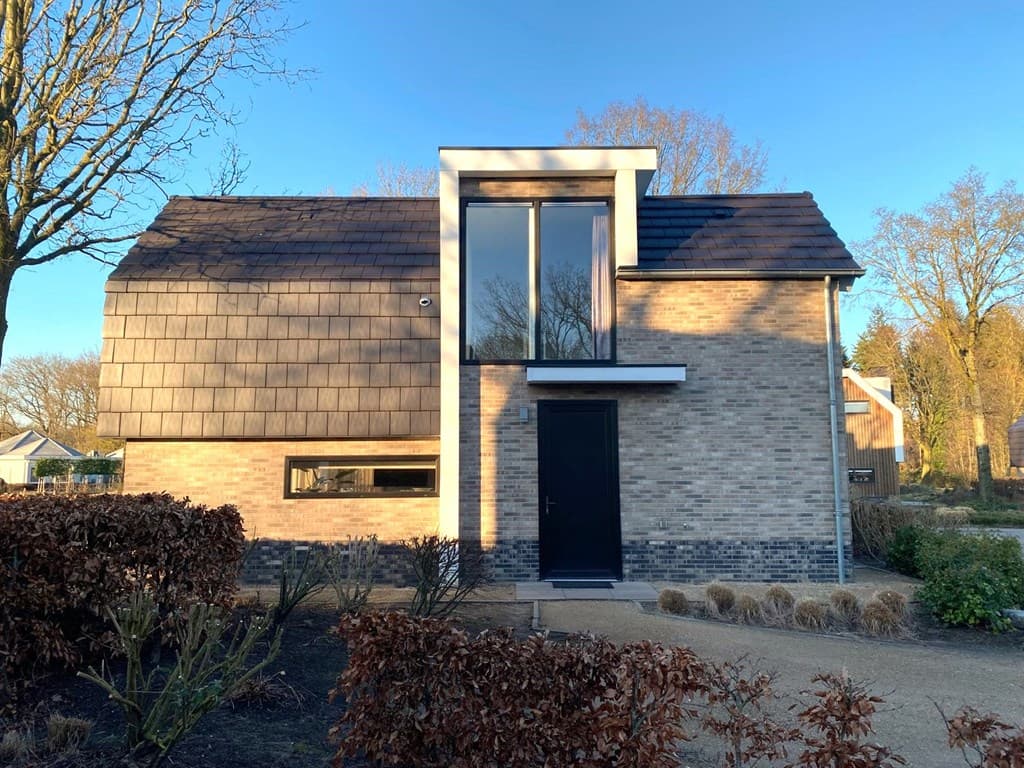 Moderne woning met een unieke gevel en grote ramen, omringd door groen en struiken in een rustige omgeving