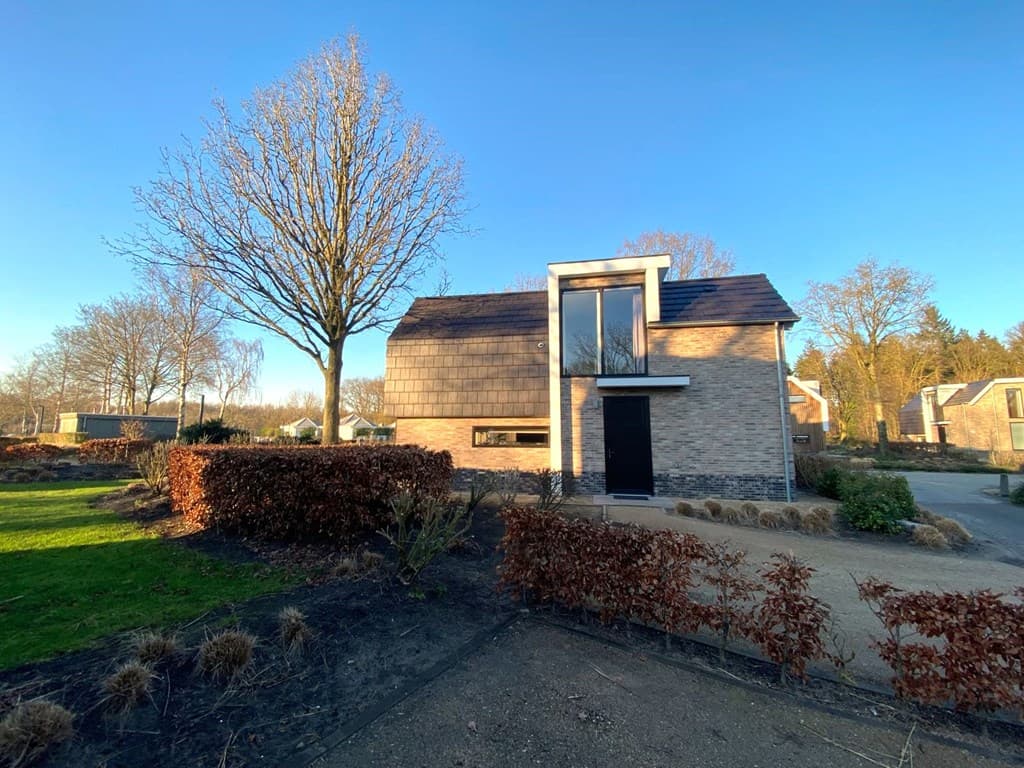Moderne woning met een combinatie van steen en hout, gelegen tussen bomen en struiken op een rustige locatie