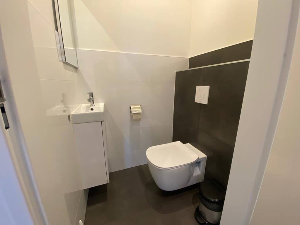 Witte wc met fonteintje en spiegel in een moderne, kleine badkamer met donkere wand- en vloertegels