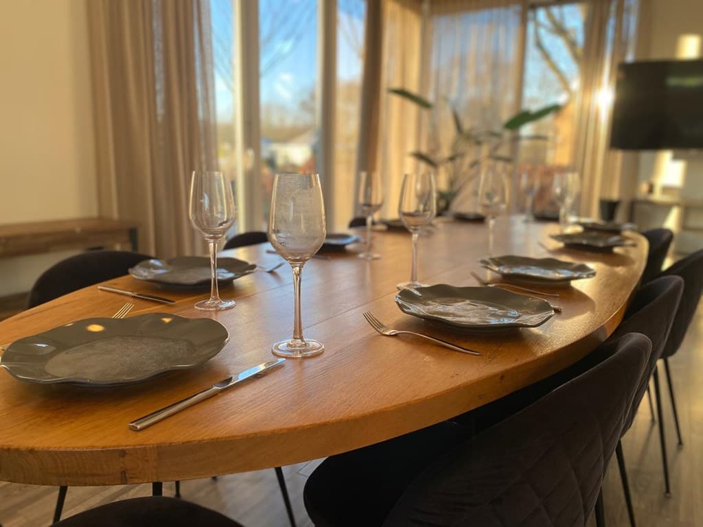 Eettafel met zwarte borden en glazen in een lichte ruimte met grote ramen en een plantenbak op de achtergrond