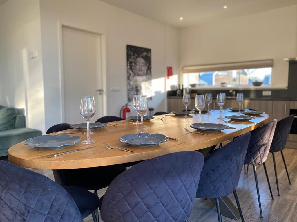 Eettafel met zes stoelen, gedekt met borden en glazen, in een lichte en moderne ruimte met keuken in de achtergrond
