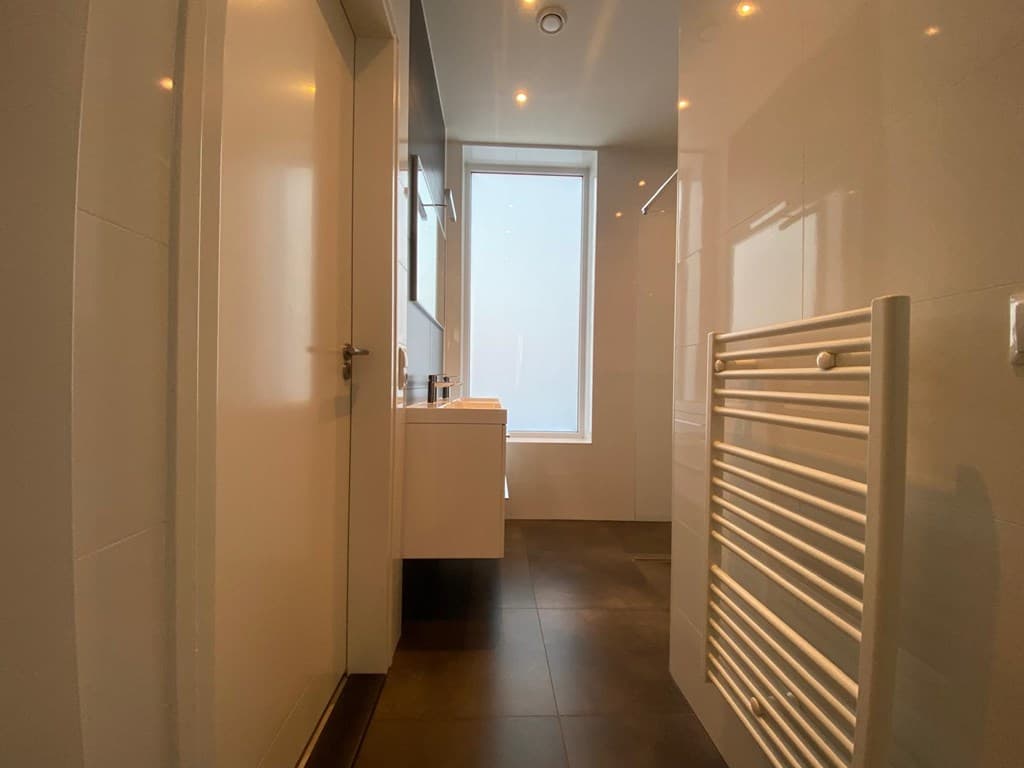 Moderne badkamer met een grote raampartij, witte tegels en handdoekradiator aan de muur.