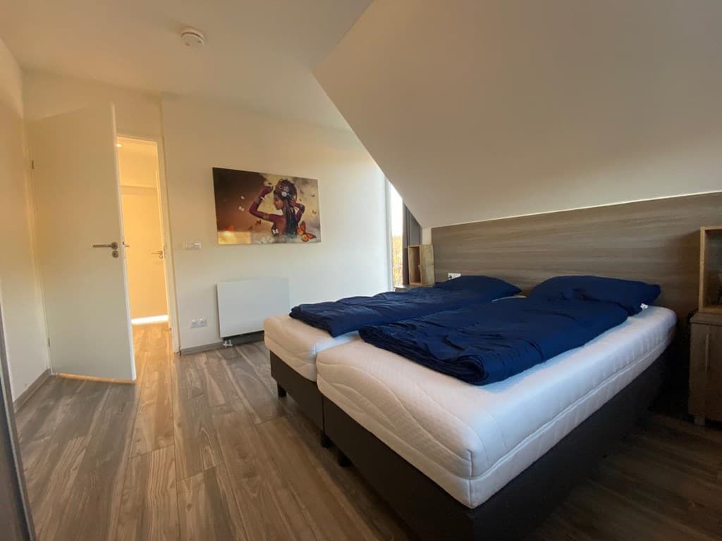 Slaapkamer met twee eenpersoonsbedden en een kunstwerk aan de muur, deur naar de gang zichtbaar.