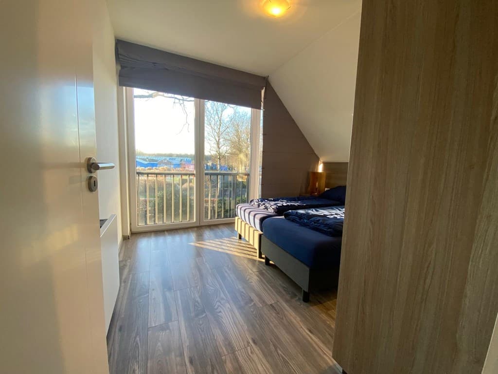 Slaapkamer met grote ramen, dubbele bed en houten vloer, uitzicht op de buitenomgeving.
