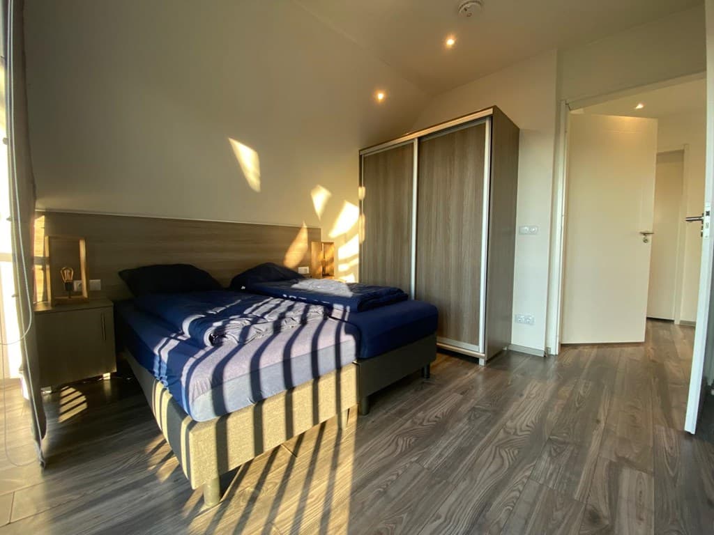 Slaapkamer met bed, kledingkast en natuurlijk licht dat door het raam valt op de houten vloer