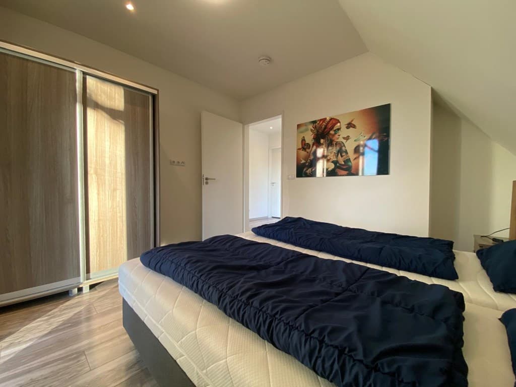 Slaapkamer met twee bedden, kastenwand, deur naar gang en kunstwerk aan de muur. Lichtinval vanuit het raam.