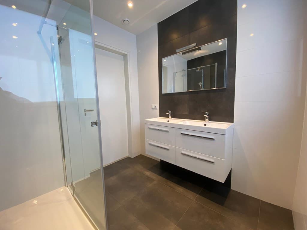 Moderne badkamer met dubbel wastafelmeubel, grote spiegel en inloopdouche in lichte en donkere tinten.