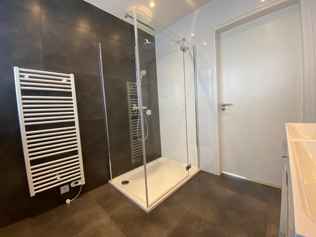 Moderne badkamer met inloopdouche, radiator en wastafel met grote spiegel aan de wand