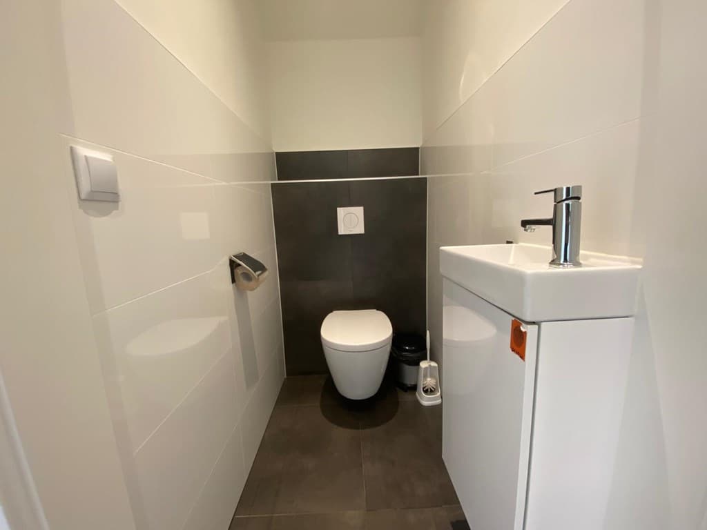 Modern toilet met witte wandtegels en donkere vloertegels, een hangtoilet en een met moderne kraan.