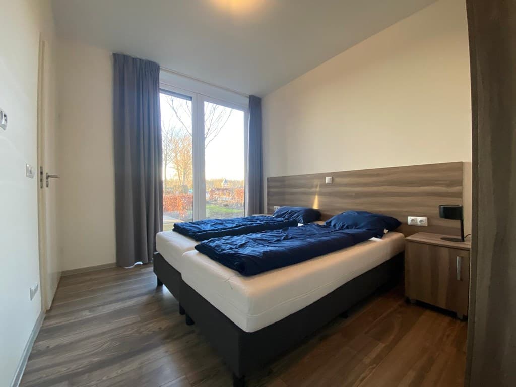 Slaapkamer met twee eenpersoonsbedden, uitzicht op de tuin en houten vloer, grote ramen met gordijnen