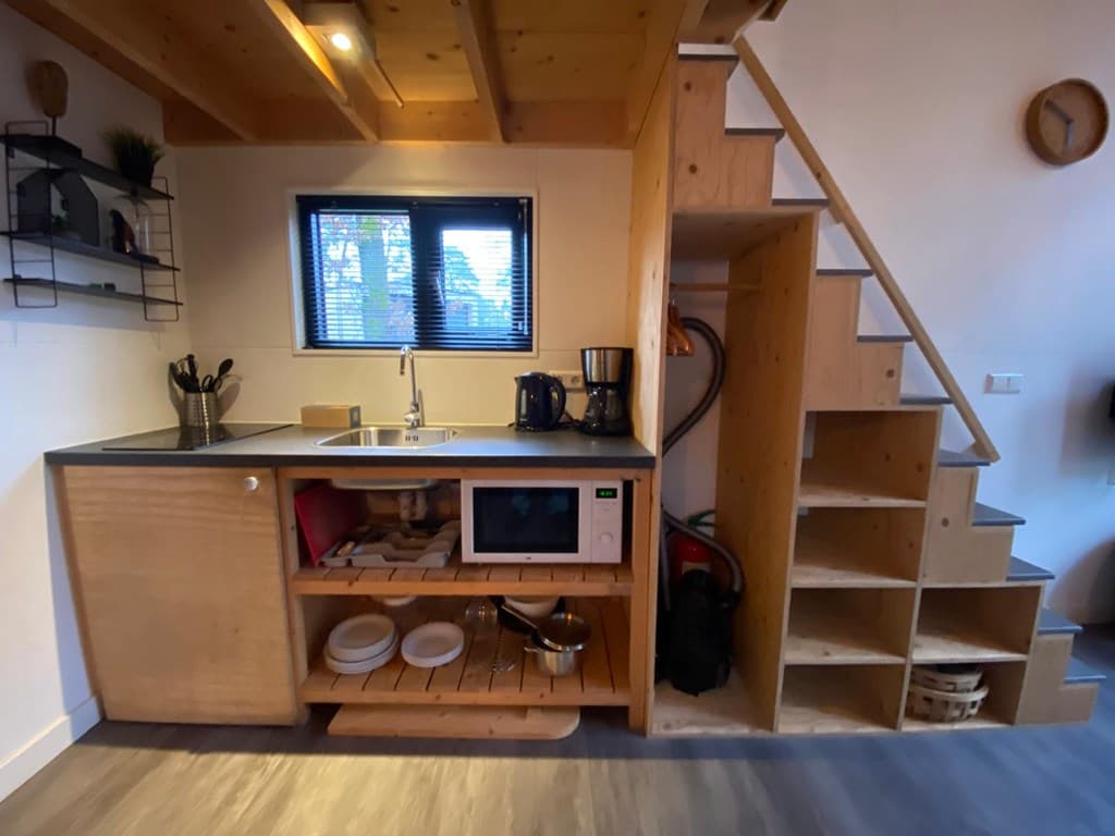 Moderne open keuken met houten kastjes, aanrechtblad, magnetron en trap naar de bovenverdieping.