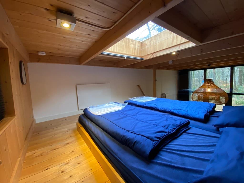 Slaapkamer met houten wanden, twee eenpersoonsbedden, een groot raam en een hanglamp van bamboe.