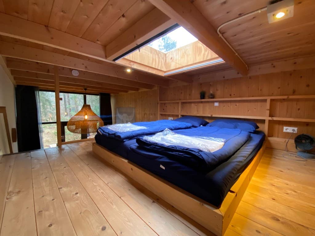 Slaapkamer met houten wanden, twee bedden met dekbedden en een dakraam voor natuurlijk licht.