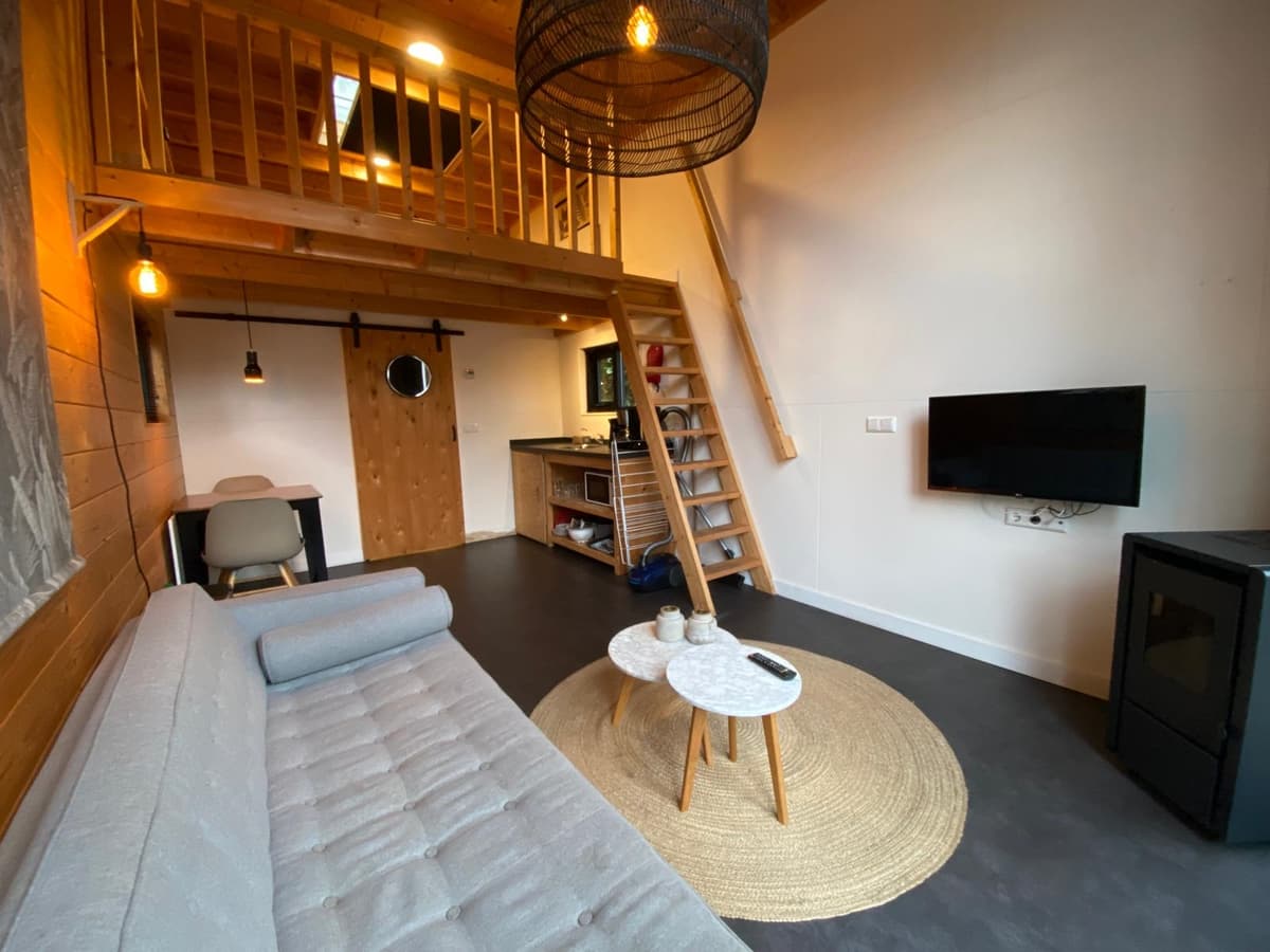 Ruime woonkamer met moderne inrichting, open trap naar vide, kitchenette en tv aan de muur.