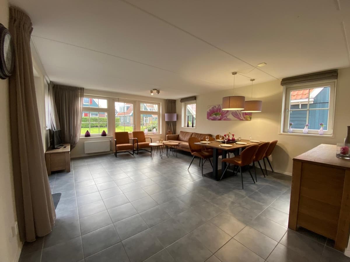 Ruime woonruimte met grote ramen, zithoek, eettafel en moderne inrichting, voorzien van neutrale kleuren en lichte meubels