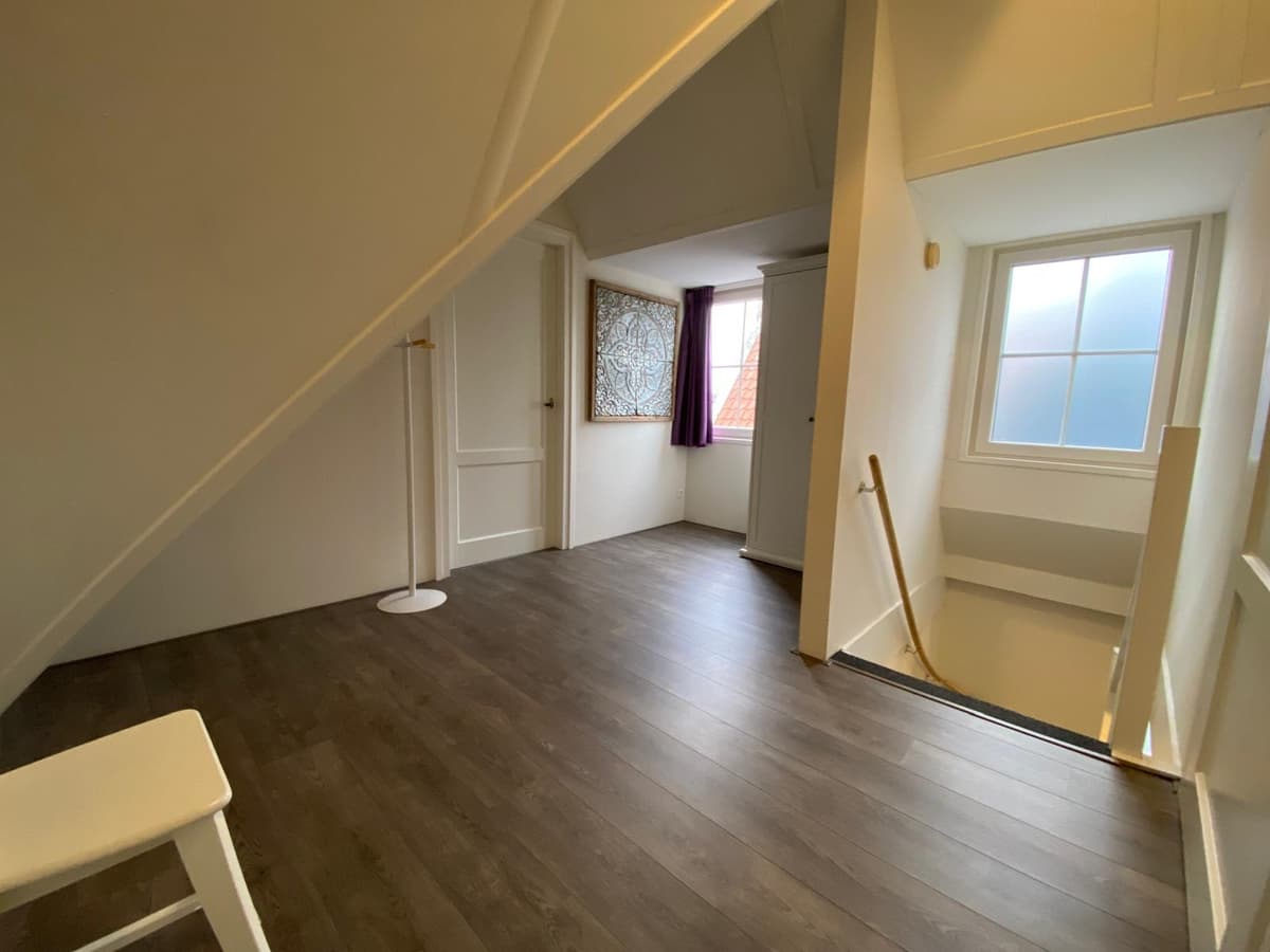 Ruime traphal met een houten vloer, venster met zicht naar buiten en een trap naar de onderverdieping