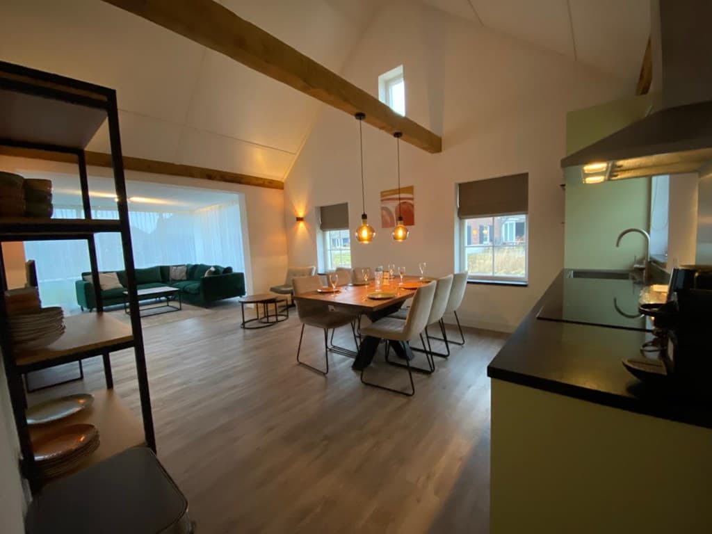 Ruimtelijk interieur met eettafel, moderne keuken en zithoek met groene bank en grote ramen.