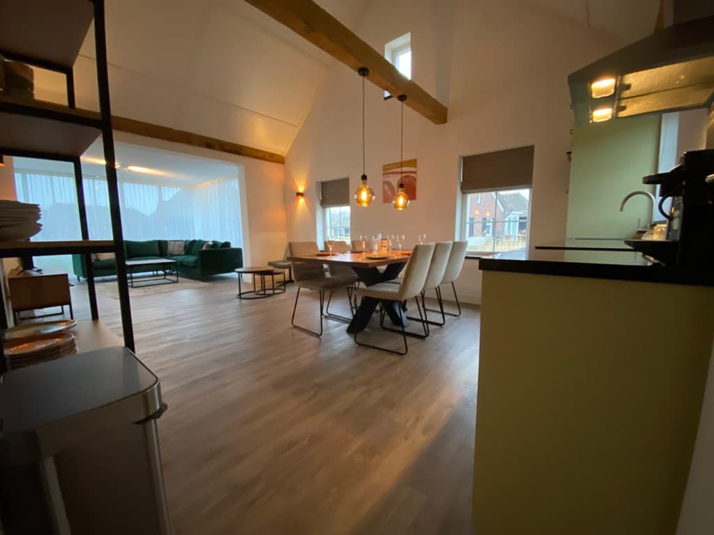 Ruime eetkamer met een grote tafel, stoelen, open keuken en uitzicht op de woonkamer met een groene bank