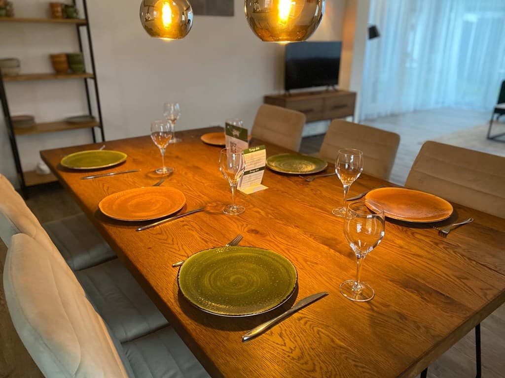 Eetkamer met een houten tafel, zes stoelen en gedekte borden in groene en oranje kleuren met een warm licht.